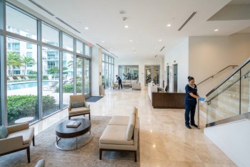 Cleaner wiping stair railing in a condominium lobby with pool view